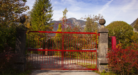 Red iron gate at the entrance to Park am See glamping accommodation in Obertraun, Austria, with mountains.