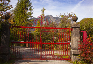 Portail en fer rouge à l'entrée du glamping Park am See à Obertraun, Autriche, entouré de verdure.