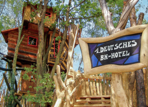 Un hotel casa sull'albero immerso tra gli alberi, con un'insegna che promuove alloggi sugli alberi tedeschi.