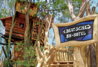 Un hotel casa sull'albero immerso tra gli alberi, con un'insegna che promuove alloggi sugli alberi tedeschi.