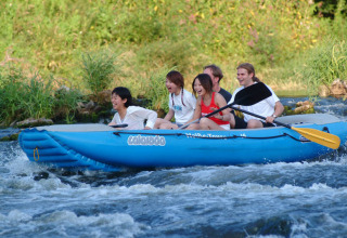 A group of friends rafting in a blue inflatable boat on a river at Het Culturele Eiland Einsiedler in Saxony.
