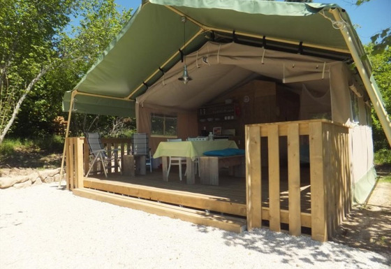 Tente safari Glamping Chave Grande avec terrasse en bois et mobilier d'extérieur sous un ciel ensoleillé.