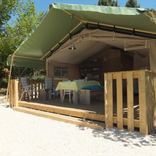 Alloggio tenda safari Glamping Chave Grande con terrazza in legno e arredi da esterno al sole.