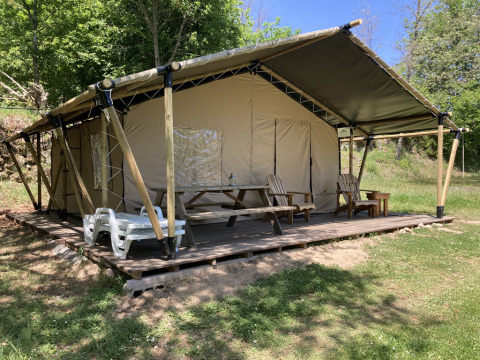 Glamping Chave Grande - Safaritenten: En luksus teltlejr med trædæk, stole og picnicbord i grønne omgivelser.