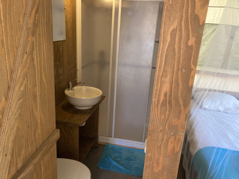 Interior of Glamping Chave Grande - Safaritenten showing shower, sink, and bed with a white mosquito net.