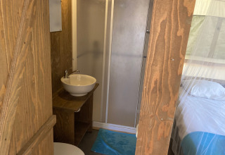 Interior of Glamping Chave Grande - Safaritenten showing shower, sink, and bed with a white mosquito net.