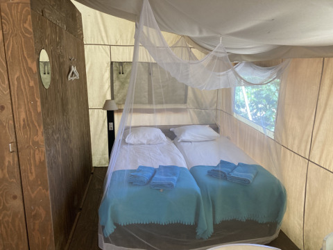 Interieur van een safaritent bij Glamping Chave Grande met twee eenpersoonsbedden, klamboe en houten kast.