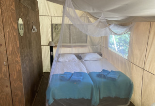 Interieur van een safaritent bij Glamping Chave Grande met twee eenpersoonsbedden, klamboe en houten kast.