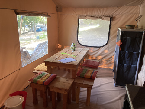 Indretning af et glamping safari-telt med træbord, farverige hynder og udsigt til naturen udenfor.