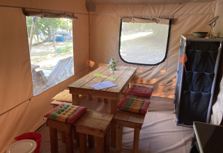 Indretning af et glamping safari-telt med træbord, farverige hynder og udsigt til naturen udenfor.