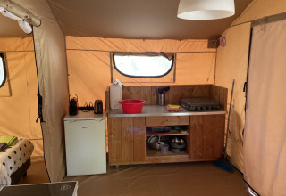 Cozy interior of Glamping Chave Grande safari tent featuring kitchenette, mini fridge, and stove.