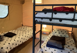 Vue intérieure d'une tente Glamping Chave Grande - Safaritenten avec lits superposés et lits simples à pois.
