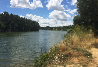 View of the river at Glamping Chave Grande - Safaritenten with trees and a summer sky with clouds.
