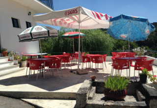 Buitenterras van Glamping Chave Grande - Safaritenten met rode stoelen, parasols en groene omgeving.