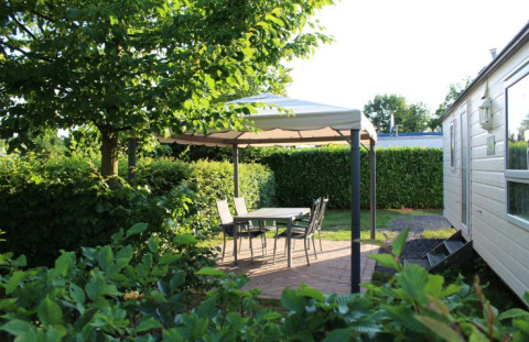 Glamping area at Campingpark Heidewald with canopy, garden table, chairs, and lush greenery outdoors.