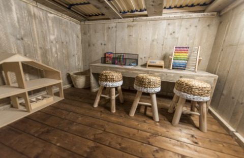 Sala giochi in legno con sgabelli intrecciati, scrivania, abaco e casa delle bambole al Campingpark Heidewald.