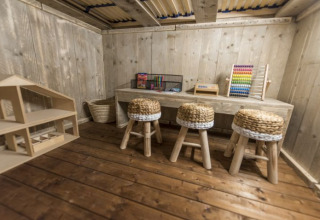 Sala de juegos de madera con taburetes, escritorio, ábaco y casa de muñecas en Campingpark Heidewald.