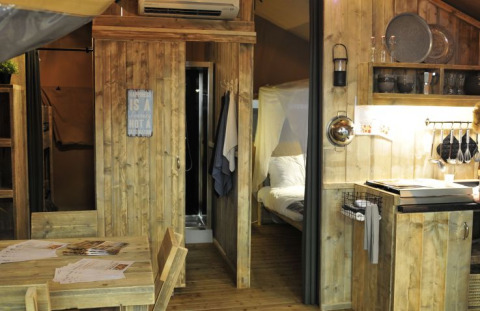 Vista interior de una tienda glamping de madera con cocina, comedor y dormitorio en Campingpark Heidewald.
