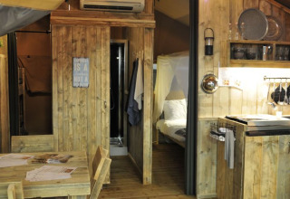 Vue intérieure d'une cabane glamping en bois avec cuisine, coin repas et chambre au Campingpark Heidewald.