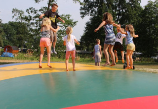 Bambini saltano e giocano su un grande cuscino colorato al Campingpark Heidewald con alberi sullo sfondo.