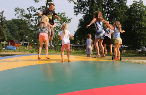Kinderen springen en spelen op een groot kleurrijk luchtkussen bij Campingpark Heidewald, tussen de bomen.