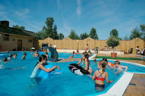 Children playing in an outdoor swimming pool at Camping en vakantiepark Wulfener Hals under blue skies.