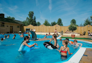 Bambini che giocano in piscina all'aperto al Camping en vakantiepark Wulfener Hals sotto un cielo blu.