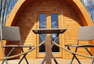Alloggio glamping 'Nord-Ostsee Camp - Pods Schleswig-Holstein' con due sedie e un tavolo davanti a una cabina di legno.
