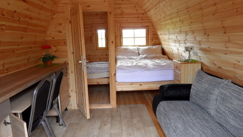 Interior view of a cozy wooden pod with double bed, desk, and sofa at Nord-Ostsee Camp accommodation.