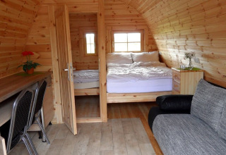 Vista interior de una cómoda cabaña de madera con cama doble, escritorio y sofá en Nord-Ostsee Camp.
