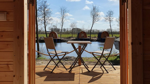 View from wooden cabin with table and two chairs overlooking lake and glamping pods at Nord-Ostsee Camp.