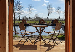 Udsigt fra træhytte med bord og to stole til sø og glamping pods hos Nord-Ostsee Camp i Slesvig-Holsten.