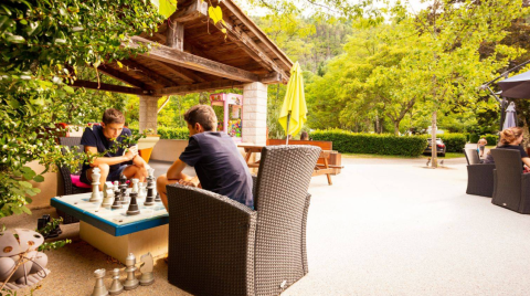 Two people play chess outdoors under a shelter at Camping Les Drouilhedes - Tent Lodges Occitanië.