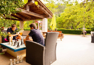 Dos personas juegan ajedrez al aire libre bajo un refugio en Camping Les Drouilhedes - Tent Lodges Occitanië.