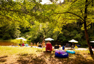 Camping Les Drouilhedes in Occitania: persone rilassate sul fiume con ombrelloni, sedie e gonfiabili da piscina.