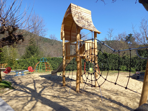 Playground with wooden climbing frame and slide at Camping Les Drouilhedes - Tent Lodges Occitanië on sunny day.