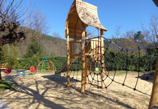Playground with wooden climbing frame and slide at Camping Les Drouilhedes - Tent Lodges Occitanië on sunny day.