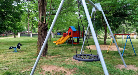 Aire de jeux avec balançoires, toboggan et maisonnette entourée d’arbres au Camping Les Drouilhedes - Tent Lodges Occitanië.