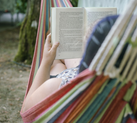 Person relaxing in a hammock while reading a book at Camping Les Drouilhedes - Tent Lodges Occitanië.