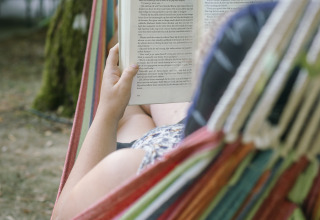 Personne se détendant dans un hamac et lisant un livre au Camping Les Drouilhedes - Tent Lodges Occitanië.