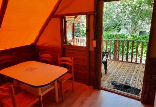 Vista interior de un lodge glamping en Camping Les Drouilhedes, con mesa, sillas y terraza exterior.