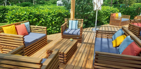 Gemütliche Holzterrasse mit Sitzmöbeln und bunten Kissen bei Camping Les Drouilhedes Tent Lodges Occitanië.