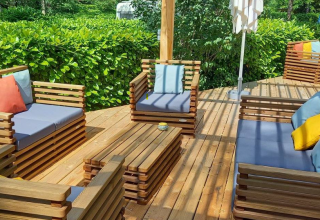 Gemütliche Holzterrasse mit Sitzmöbeln und bunten Kissen bei Camping Les Drouilhedes Tent Lodges Occitanië.