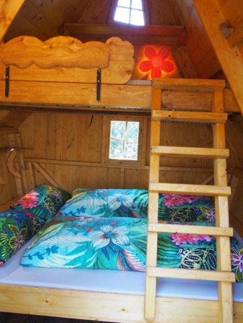 Innenansicht einer gemütlichen Baumhütte im Familiepark Sottrum mit buntem Bettzeug und Hochbett.