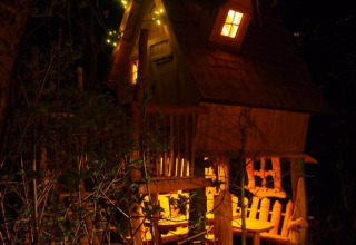 Verlichte boomhut in Familiepark Sottrum Boomhutten Nedersaksen, glamping in het bos bij nacht in Vlaanderen.