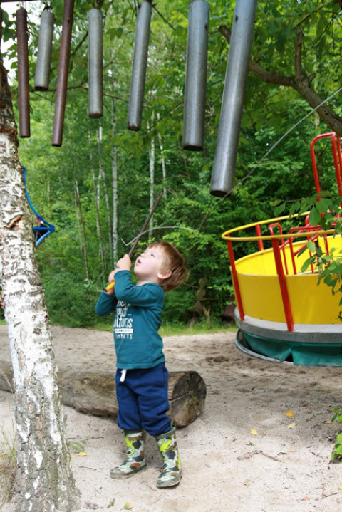 Kind speelt met windgongen in Familiepark Sottrum - Boomhutten Nedersaksen, omringd door natuur.