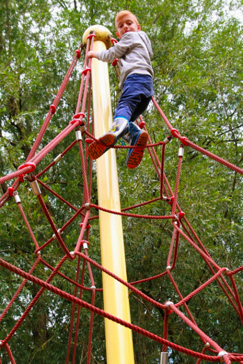 Junge klettert auf einem Seilnetz im Familiepark Sottrum Boomhutten Nedersaksen, umgeben von grüner Natur.