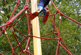 Bambino che scala una rete di corde al Familiepark Sottrum Boomhutten Nedersaksen durante esperienza campeggio.