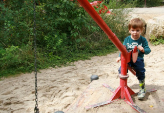 Kind speelt met een zandgraafmachine op de speeltuin in Familiepark Sottrum - Boomhutten Nedersaksen.