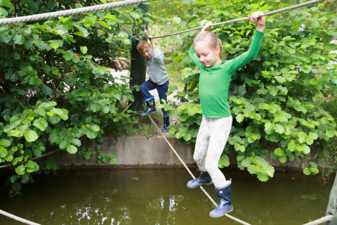 Due bambini in equilibrio su una corda sopra l'acqua al Familiepark Sottrum, Boomhutten glamping, Bassa Sassonia.